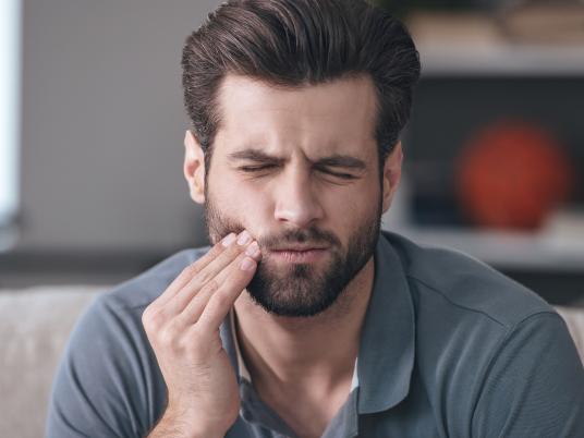 Mann hält sich schmerzverzogen den Kiefer