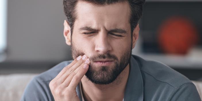 Mann hält sich schmerzverzogen den Kiefer